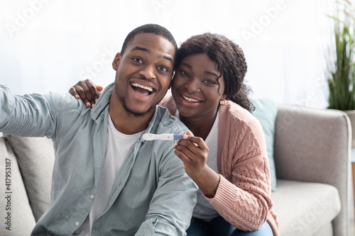 Happy black couple with positive pregnancy test taking selfie