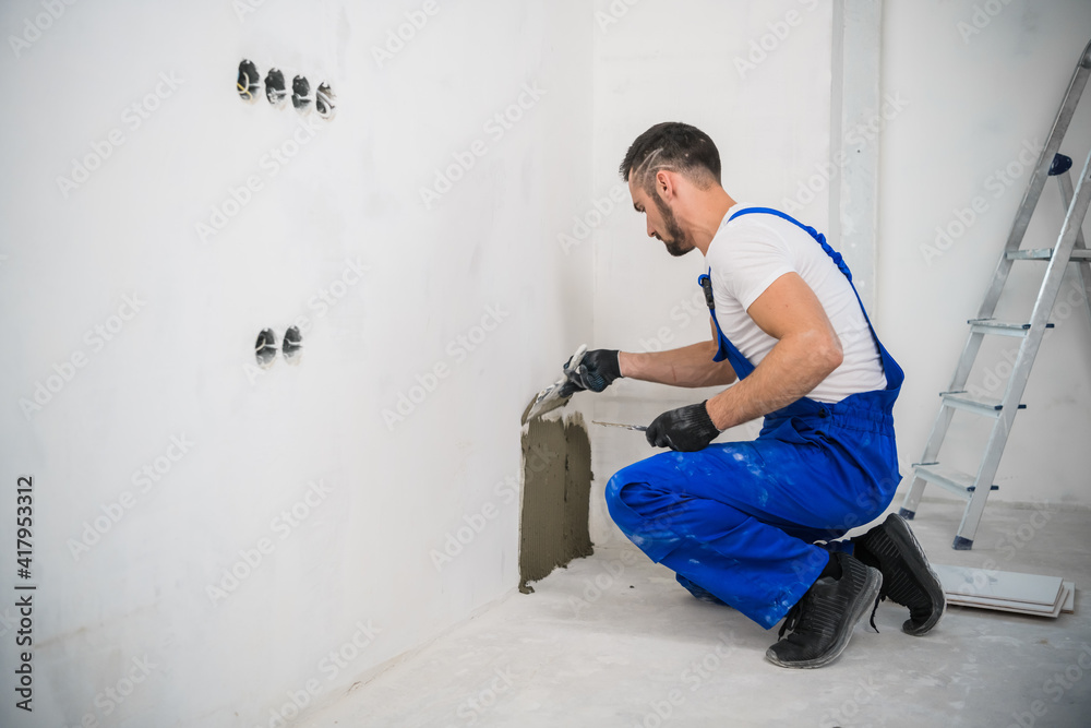 A general laborer in overalls uses a trowel to cover the wall with cement A general laborer in overalls uses a trowel to cover the wall with cement