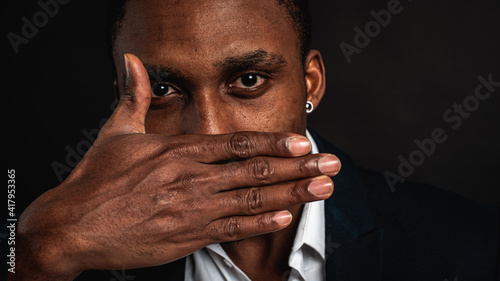Portrait of young dark-skinned student or employee looking at the camera with surprised guilty expression, doing something wrong, covering his mouth. Human face expressions and emotions. Body language