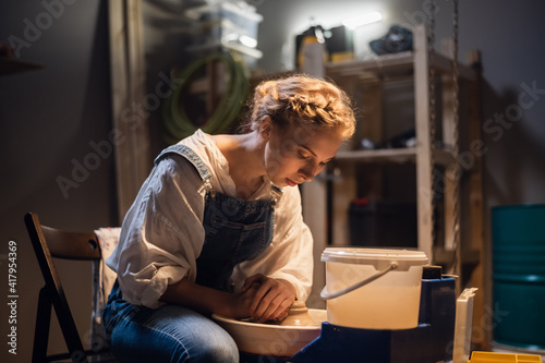 a young blonde potter girl starts making a vase in her workshop on the potter's wheel