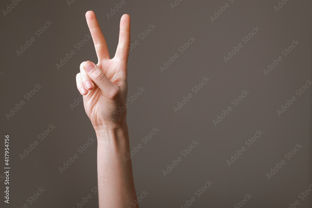 Woman hands isolated showing victory sign on grey background, gesture of victory. Policy position and belief.