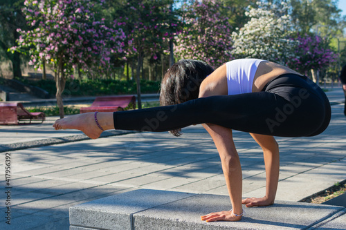 beautiful brunette fitness woman, doing yoga in the park carrying her body with her hands and stretching her legs. concept of muscle strength, stretching flexibility and balance.