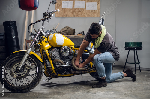 A modern young man in a t-shirt and jeans is engaged in bike diagnostics in a repair shop or garage