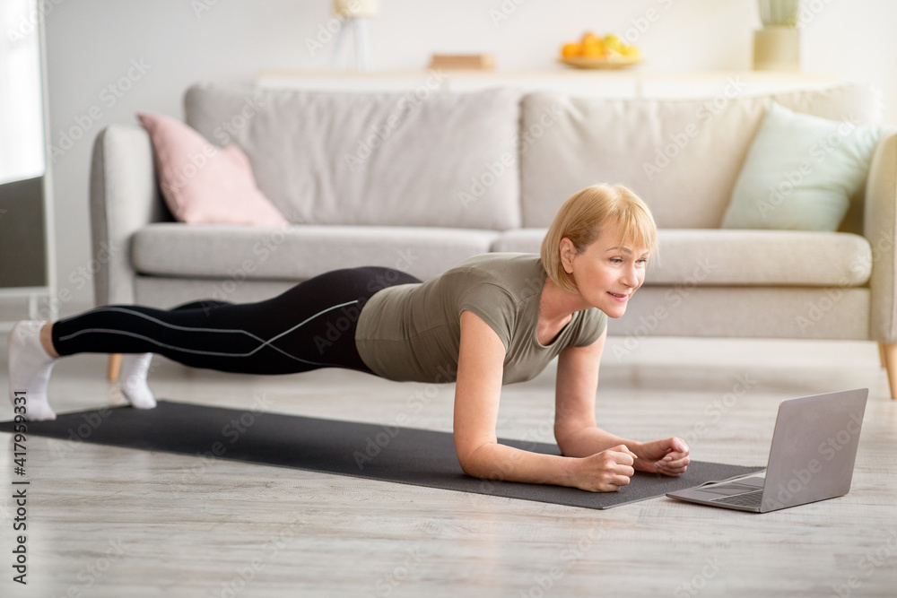 Strong senior woman standing in elbow plank on yoga mat, working out to online sports video at home Strong senior woman standing in elbow plank on yoga mat, working out to online sports video at home