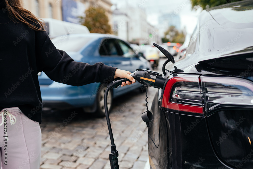 Woman near electric car. Vehicle charged at the charging station. Woman near electric car. Vehicle charged at the charging station.