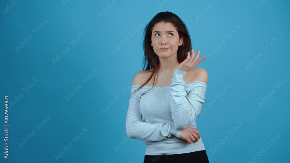 The young woman who thinks while putting her hands to her mouth, for new ideas, puzzled. Asian with dark hair, dressed in a blue blouse, isolated on a dark blue background in the studio. Lifestyle