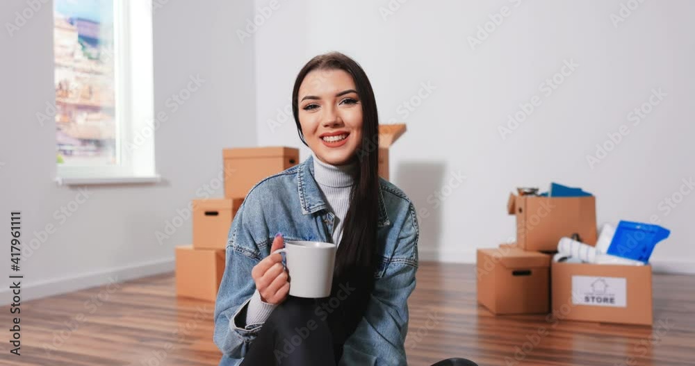 Cheerful Caucasian woman sitting on floor in living room with cup of coffee and thinkinCheerful Caucasian woman sitting on floor living room with cup of coffee and thinking about new interior