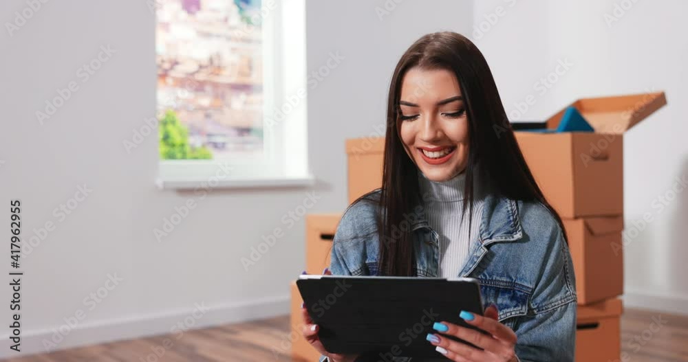 Happy beautiful young woman sitting on the floor in new apartment and thinking about future interior of room browsing catalog of interior design using tablet. Happy beautiful young woman sitting on the floor in new apartment and thinking about future interior of room browsing catalog of interior design using tablet.