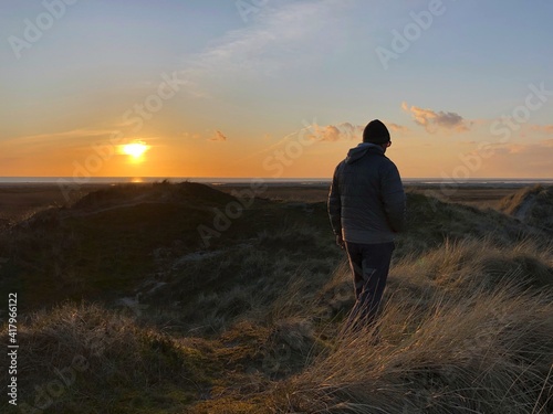 Rear view of a man walking on beach in winter at sunset, Fanoe, Jutland, Denmark photo