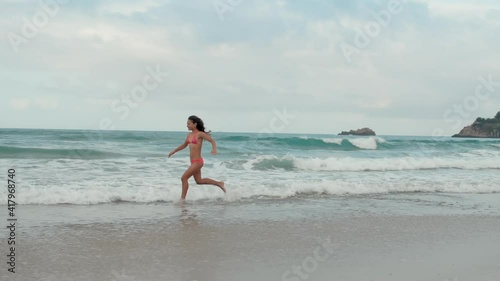 Young woman spending summer at seaside. Cheerful girl running along beach.