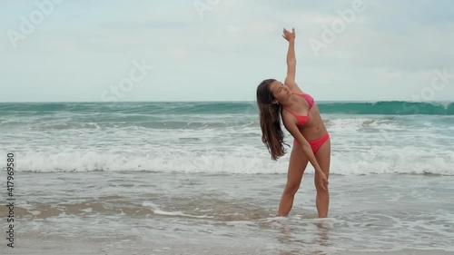 Young woman standing at seaside. Beautiful girl doing exercises at coastline.