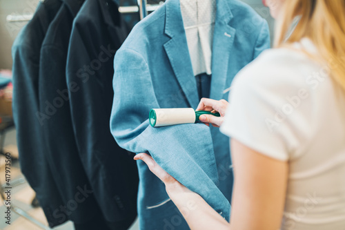 Female cleaner in laundry shop checking clean clothes, she is removing lint with roller. photo