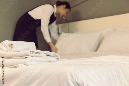 Clean fresh towels on the bed with blurred room service maid cleaning hotel room.