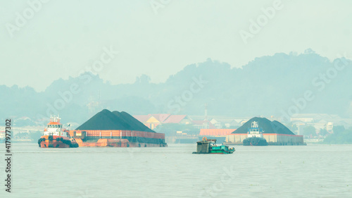 Tugboat drag barge full of coal crossing Mahakam River  Samarinda  in the morning. Transportation and industrial background