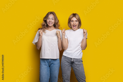 Caucasian woman are surprised by something posing on a yellow wall and gesturing with fists