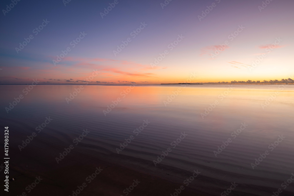 Peaceful dawn, colorful sky, smooth sea over wavy sands, island on horizon. Iriomote Island.