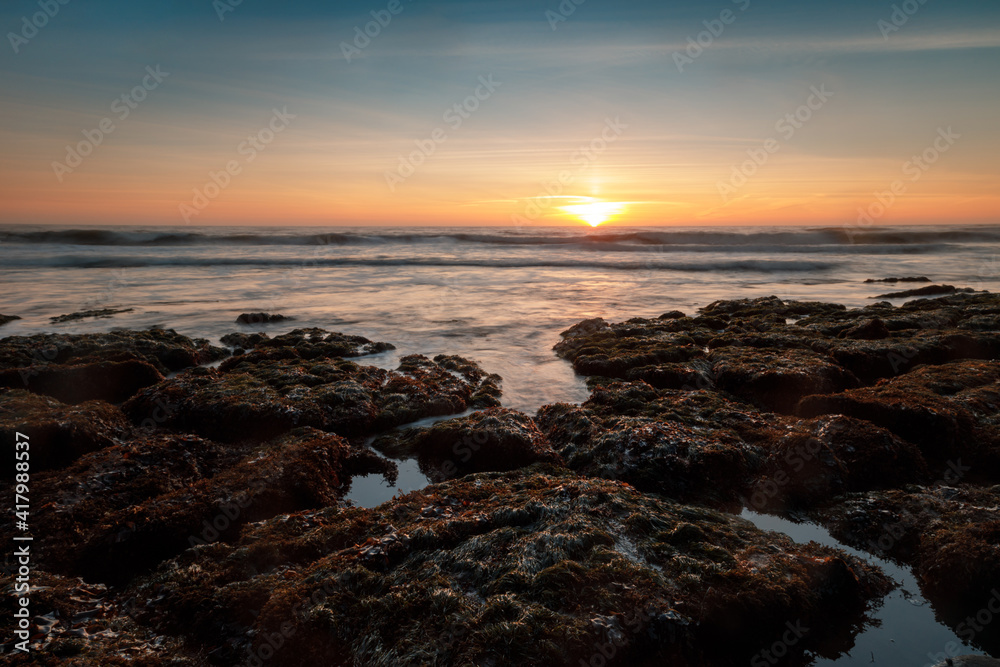 Sun setting over tide pools in the Pacific Ocean. Bean Hollow State Beach, San Mateo County, California, USA.