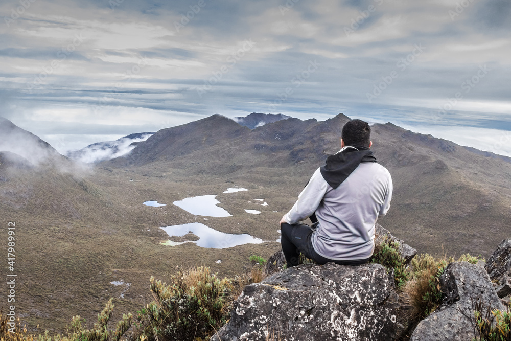 Middle-aged man sitting observing the landscape with mountains, lakes and a cloudy sky