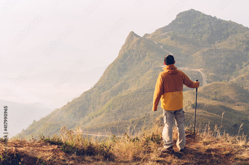 Rear view of male climber standing on mountain edge and looking to beautiful mountain peak in front of him. Conceptual of travel and adventure on mountains.