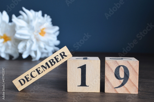 December 19, Date cover design with calendar cube and white Paeonia flower on wooden table and blue background.	
