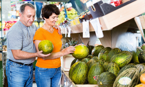 Adult cheerful male and female are choosing green melons in the store.