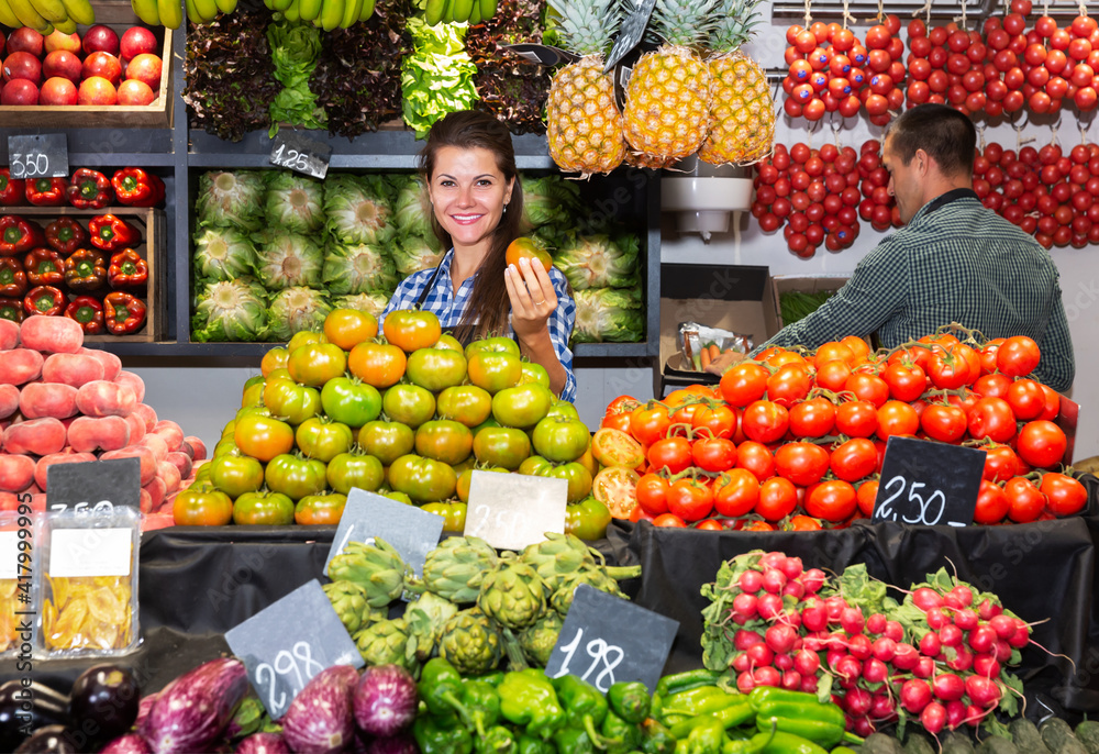 Portrait of young woman in apron selling fresh tomatoes on vegetables shop