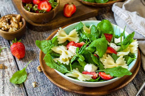 Italian pasta salad with strawberries, arugula, nuts, soft cheese dressed with balsamic sauce on the wooden table.