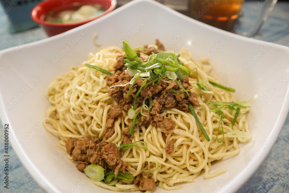 mie ayam or Noodle with chicken in white bowl on table  with chicken strip, vegetable , chili sauce and salty crispy cracker. Mie Ayam Indonesia Noodle