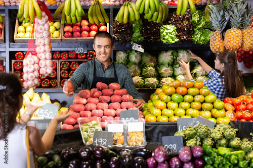 Friendly glad man and woman laying out vegetables and fruits in shop photo