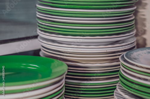 Close-up shot high stack storage of melamine plastic round white green clean flat plates after washing. Is this Kitchen dishes utensils bad, harmful to eat or safe. Cheap price or health compromise
