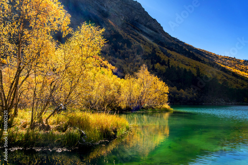 Beautiful autumn landscape with clear green water of a mountain lake and reflected trees with autumn foliage and mountain peaks