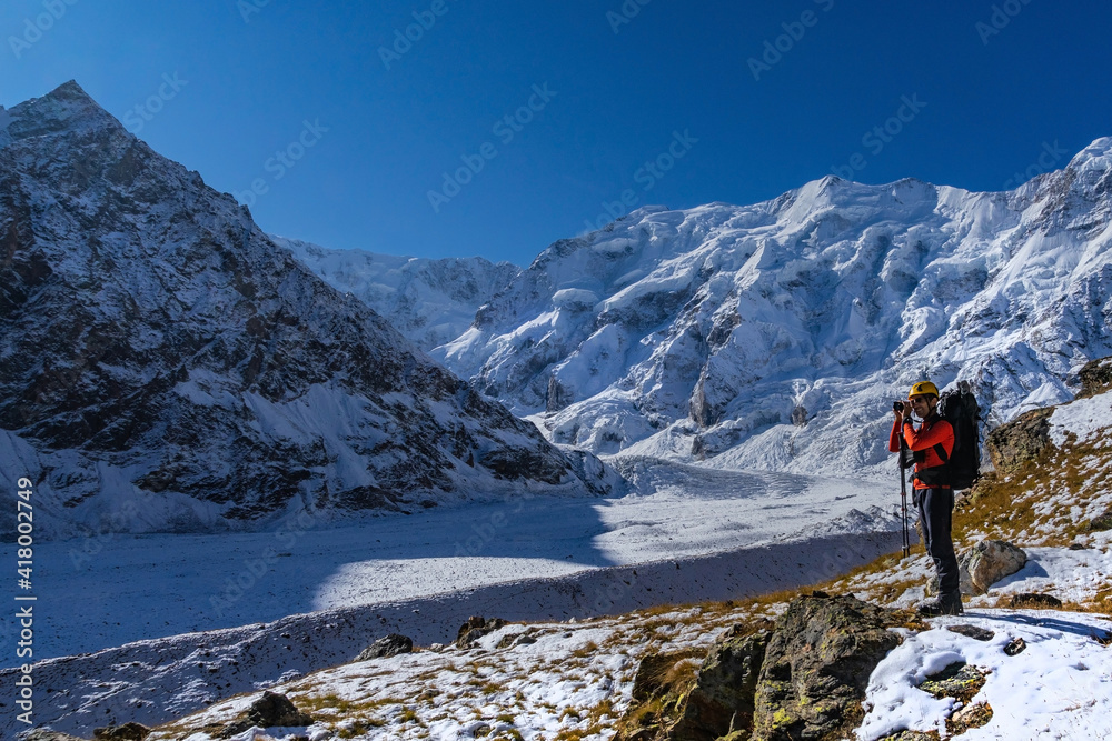 Beautiful landscape with mountains, a huge blue glacier and a silhouette of a man photographing a beautiful view against the background of mountains and glacier