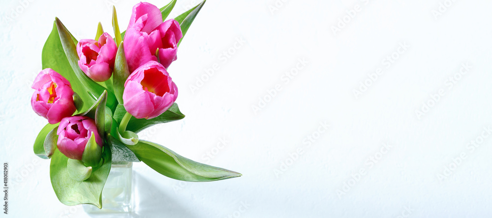 Bouquet of pink tulips in a glass vase on a light background with copy space.