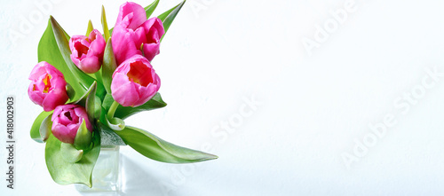 Bouquet of pink tulips in a glass vase on a light background with copy space.