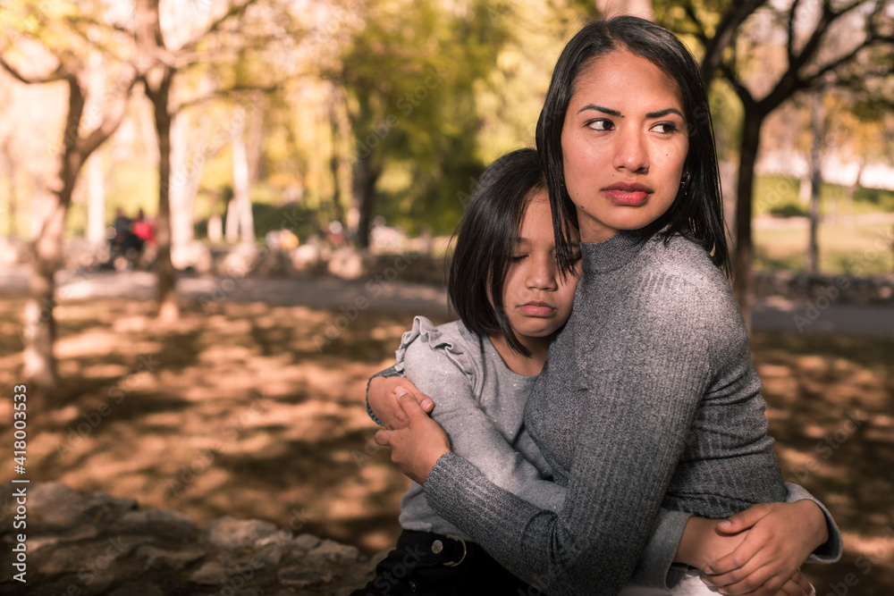 Young mother hugging and consoling her daughter outside. Looking forward protecting her little girl. Young mother hugging and consoling her daughter outside. Looking forward protecting her little girl.