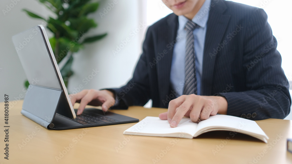Successful businessman working with tablet computer and reading information on notebook at office. Successful businessman working with tablet computer and reading information on notebook at office.