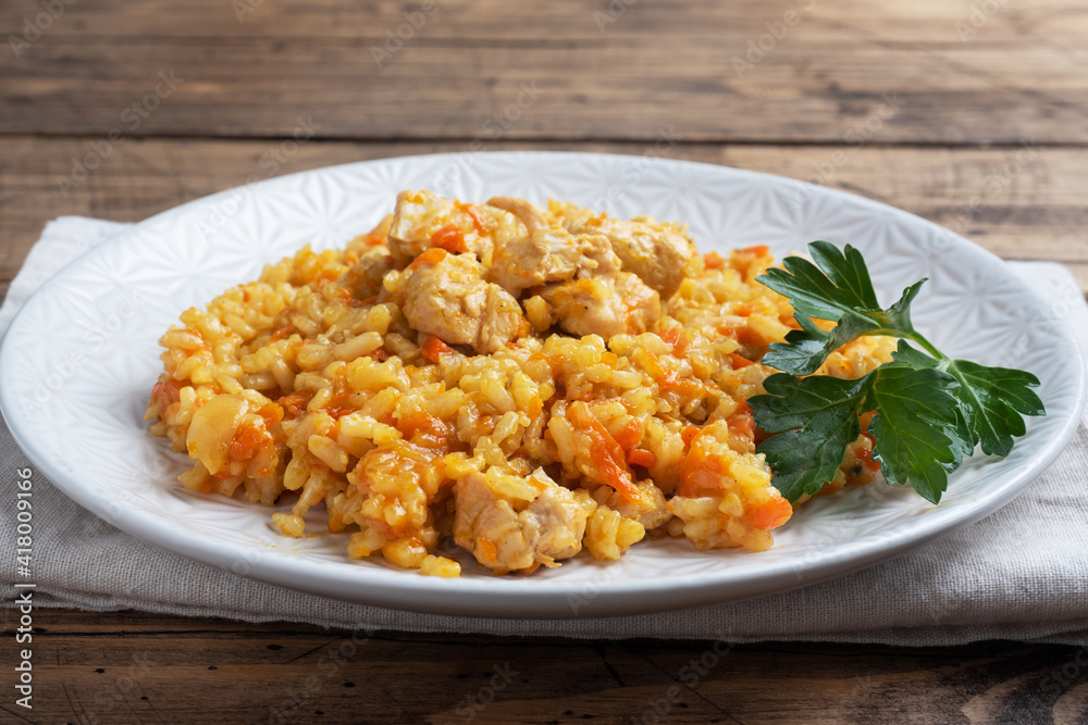 Delicious Asian pilaf, stewed rice with vegetables and chicken on a plate. Wooden rustic background. Delicious Asian pilaf, stewed rice with vegetables and chicken on a plate. Wooden rustic background.