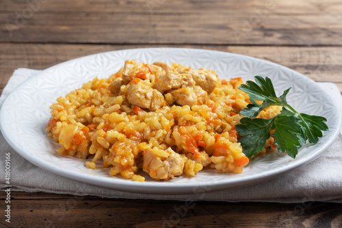 Delicious Asian pilaf, stewed rice with vegetables and chicken on a plate. Wooden rustic background.