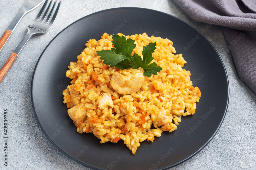 Delicious Asian pilaf, stewed rice with vegetables and chicken on a plate. gray concrete background. Delicious Asian pilaf, stewed rice with vegetables and chicken on a plate. gray concrete background.