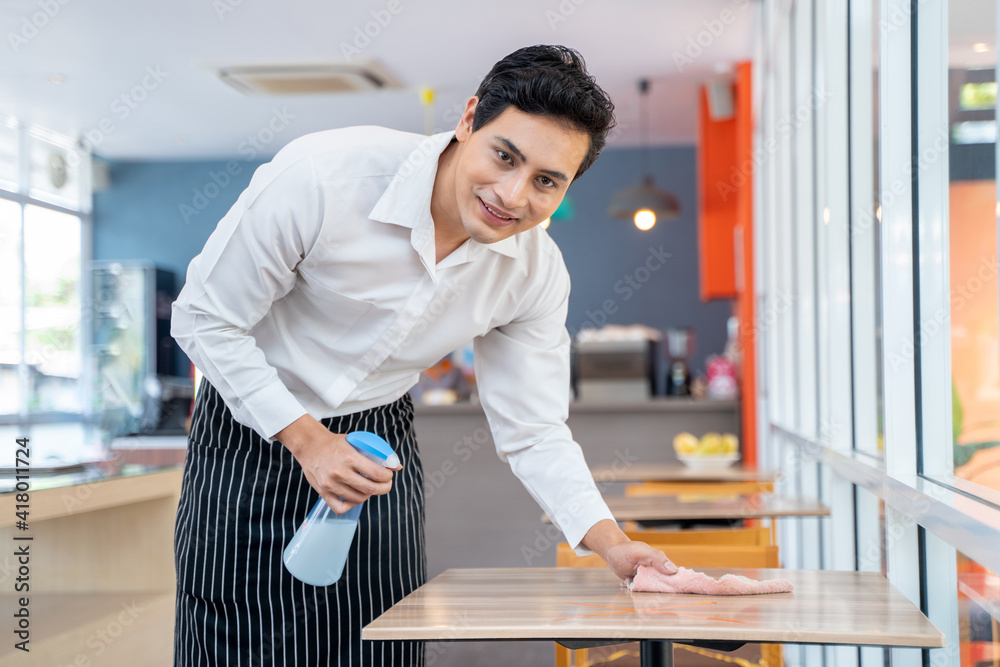 Waiter cleaning the table with Disinfectant Spray in a cafe. Stock