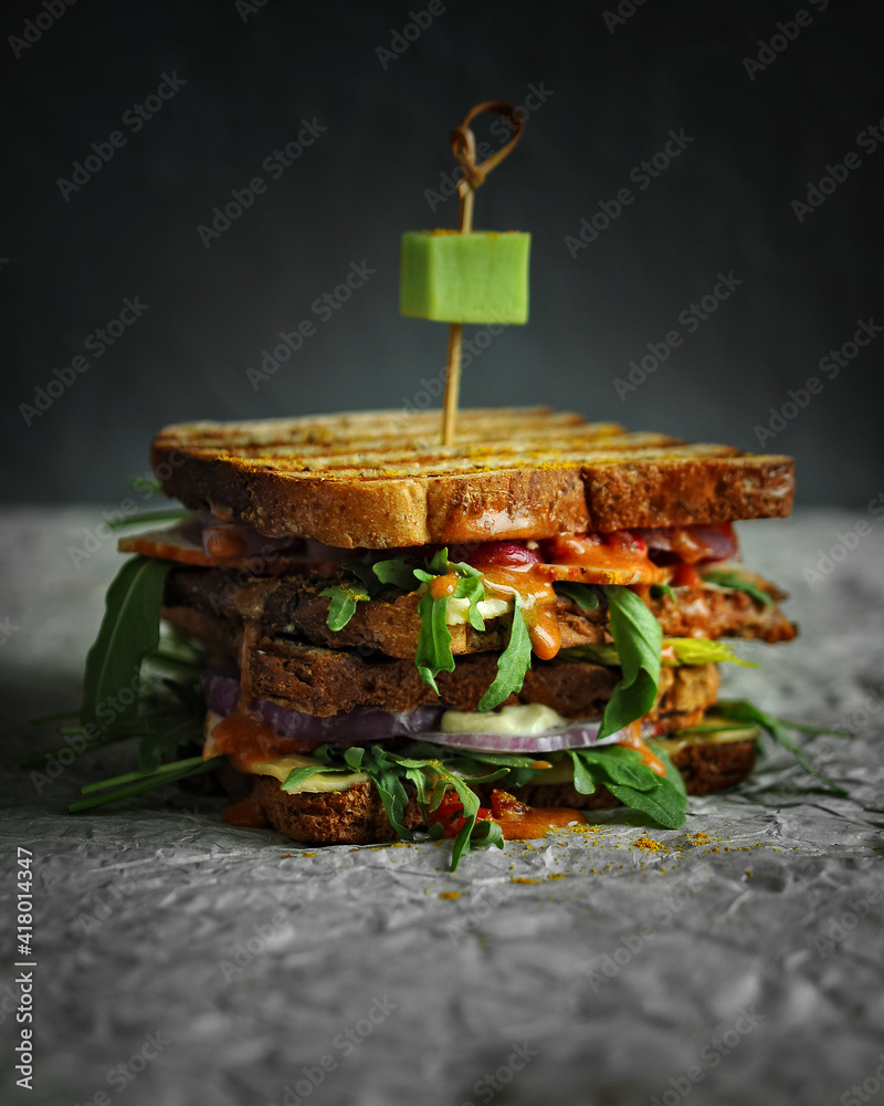 layered sandwich with toasted bread, bacon, cheese, herbs and tomato sauce on gray textured background closeup layered sandwich with toasted bread, bacon, cheese, herbs and tomato sauce on gray textured background closeup