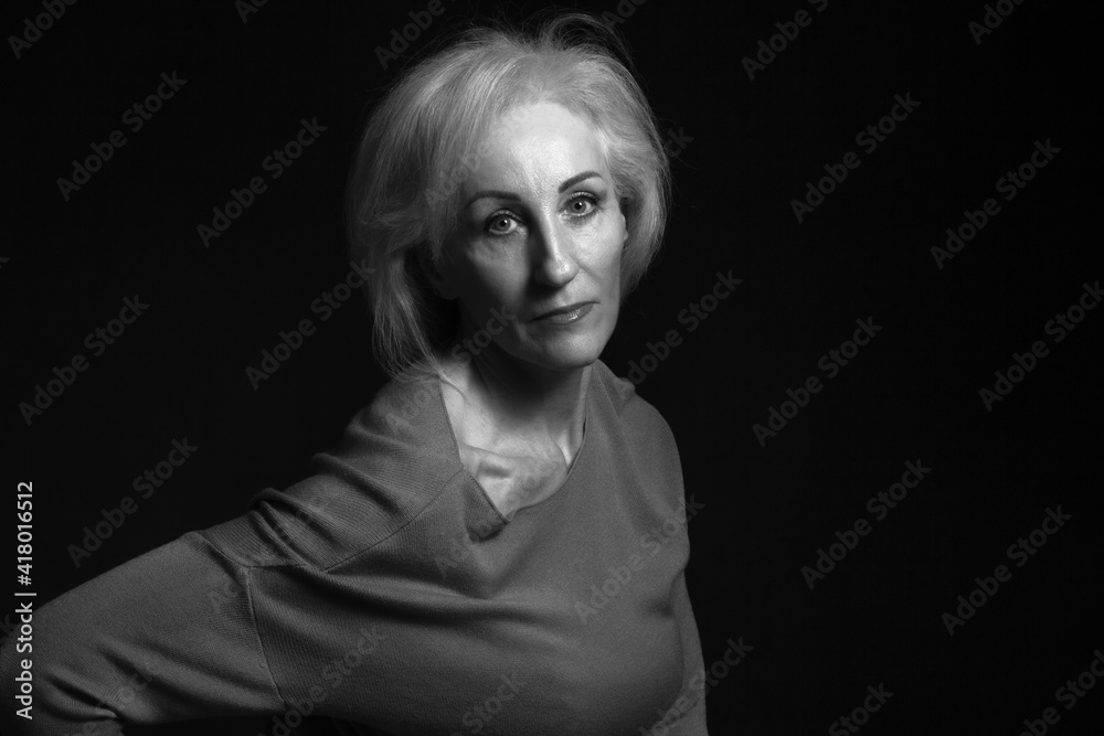 Classic black-and-white dramatic portrait of elderly blonde woman in Studio on black background