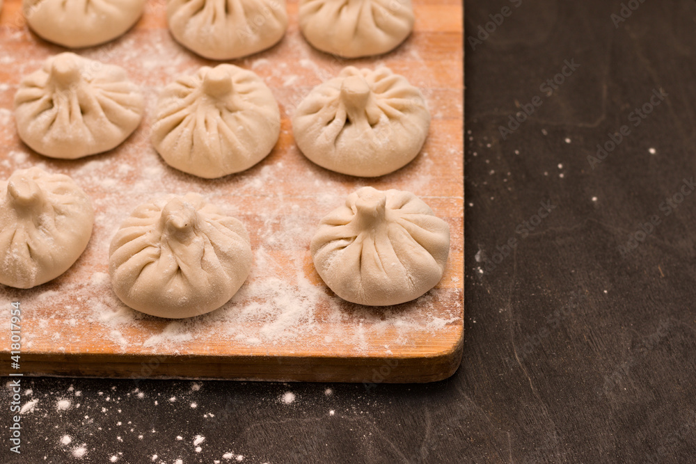 Smooth rows of raw Georgian khinkali crushed by flour lying on the corner of a kitchen board