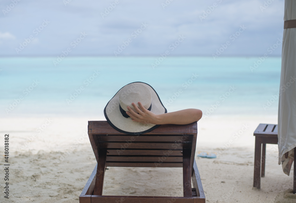 The girl wearing hat and lying down on beach chair