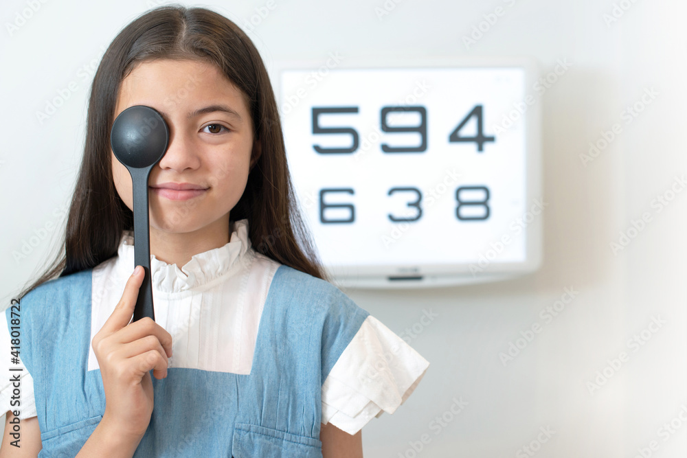 Child girl uses occluder to cover one of her eyes for vision test, eyes test monitor in the background Child girl uses occluder to cover one of her eyes for vision test, eyes test monitor in the background