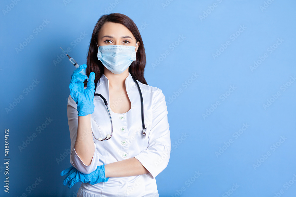 The girl is a doctor in gloves and a mask holding a syringe. The concept of vaccination. Portrait on a blue background. Covid-19. space for text and advertisements