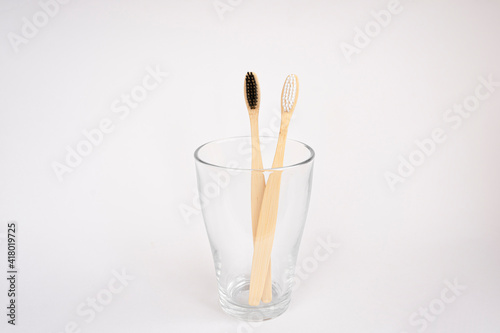 Natural wooden bamboo toothbrushes in a glass on a white background. Oral and gum care concept. Recyclable natural organic toothbrush. Flat lay, top view, copy space for text