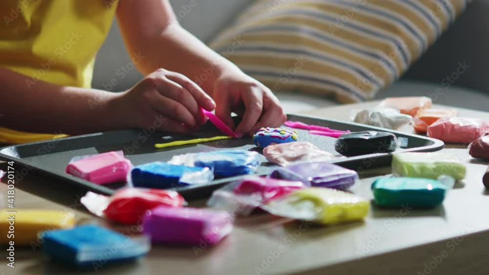 Skillful child is sculpting a doughnut from colorful plasticine, rolling piece of yellow plasticine and cutting it with small plastic knife, creative activity, Close up, Slow motion. Skillful child is sculpting a doughnut from colorful plasticine, rolling piece of yellow plasticine and cutting it with small plastic knife, creative activity, Close up, Slow motion.