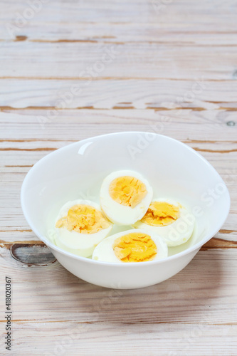 Hard-boiled eggs in a white bowl on wooden table.