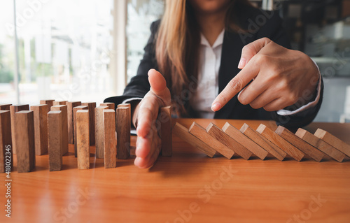 Businesswoman hand stopping the domino wooden effect concept for business and risk.